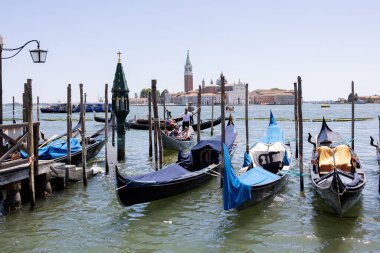 İtalya, Venedik 'teki San Giorgio Maggiore adasının sakin bir manzarası. İkonik kilise ve çan kulesi açık mavi gökyüzüne karşı yükseliyor. Venedik Gölünün sakin sularında ilerleyen bir motorlu tekne ön planda.