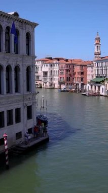 İtalya, Venedik 'teki Büyük Kanal' ın çarpıcı bir görüntüsü, açık mavi gökyüzü altında kayıkların, gondolların ve deniz kenarındaki kafelerin canlı aktivitelerini gözler önüne seriyor.