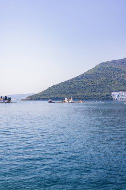 Karadağ 'ın Kotor Körfezi' ndeki iki ikonik adanın çarpıcı manzarası: Kayaların Leydisi ve Aziz George. Sakin mavi sular ve yemyeşil dağlarla çevrili bu resim Adriyatik kıyılarının dingin güzelliğini ve kültürel zenginliğini yansıtıyor.
