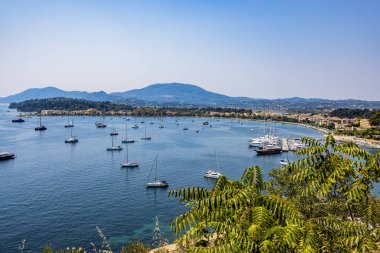 Sayısız yelkenli ve yatla benekli sakin bir körfez manzarası kayan tepeler ve yemyeşil bir zemin üzerine kurulmuş. Huzurlu su, çevresindeki manzaranın güzelliğini yansıtıyor ve huzurlu bir deniz manzarası yaratıyor.