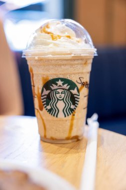Starbucks karamel frappuccino krem şantili ve karamel çiselemeli, rahat bir kafede, ahşap bir masanın üzerine yerleştirilmiş.