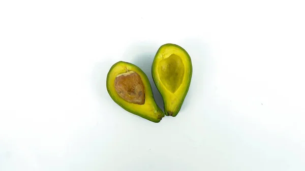 Bölünmüş ve olgunlaşmış yeşil avokado meyvesi. İnsan sağlığı için birçok vitamin içeriyor. Beyaz bir paspasın üzerine yerleştirilmiş.