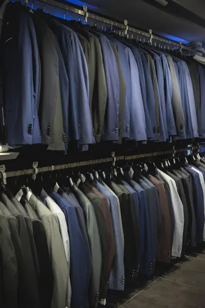 Suit jackets in hanger in men fashion and apparel store. Row of many clothes in rack or wardrobe. New stylish collection in elegant luxury retail shop. Expensive custom tailor made professional wear.