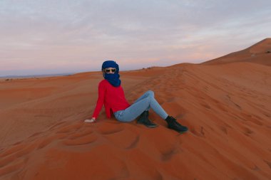 Gün batımında, Sahara 'da bir kum tepesinde berber eşarbıyla oturan genç bir kız. Yüksek kalite fotoğraf