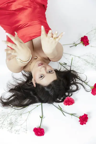 Kırmızı elbiseli ve etrafında kırmızı çiçeklerle poz veren kıvrımlı kız. Yüksek kalite fotoğraf