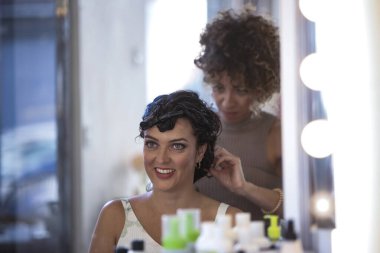 Kıvırcık saçlı müşteriyle çalışan profesyonel stilist. Profesyonel bir kuaför, müşterilerinin kıvırcık saçlarını dikkatli bir şekilde modern bir salonda şekillendirir ve uzmanlık ve özen gösterir. Yüksek kalite fotoğraf