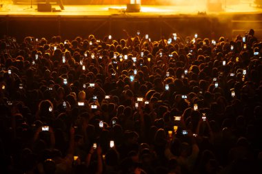 Parlak ışıklarla dolu bir konserde cep telefonlarını havaya kaldıran bir kalabalık. Yüksek kalite fotoğraf