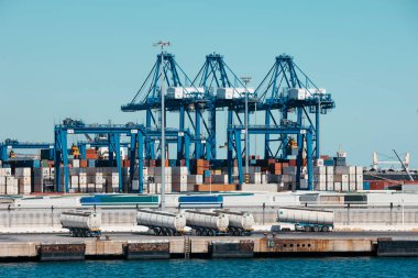 İspanya 'nın Algeciras kentindeki işlek konteyner limanı. Mavi vinçler, nakliye konteynırları ve temiz bir gökyüzünün altında yakıt tankerleri görünüyor..