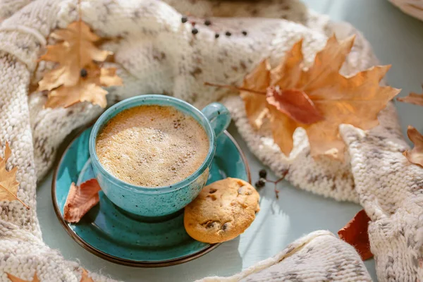 Stock image Autumnal composition with white knitted scarf, blue cup of coffee, cookies and dry yellow leaves on a table. Autumn mood.