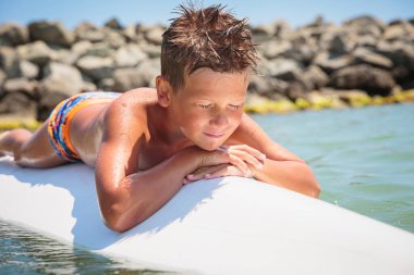 Handsome teenage boy lying on a swimming board and having fun floating on a swim board in the sea on a hot summer day