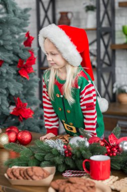 Noel Baba şapkalı çocuk, Noel kutlaması için zencefilli kurabiye hazırlıyor. Beyaz mutfakta Noel ağacıyla şeker hazırlayan kız.