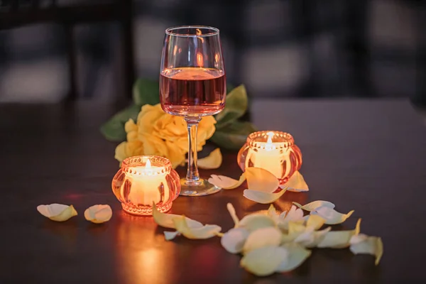 A glass of rose wine, two candles and rose petals on a dark table. Nice evening romantic atmosphere