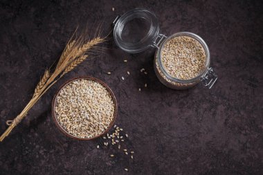 Koyu arka planda bir kase çiğ inci arpa gevreği. İnci arpa lapası pişirme kavramı.