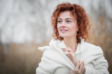 Modayı takip eden beyaz önlüklü çekici kadın portresi, sonbahar manzarasının arka planına karşı duruyor.