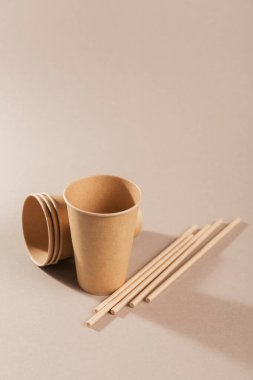 Açık bej arka planda el sanatları kağıdından yapılmış çevre dostu tek kullanımlık aletler. Kağıt bardak ve pipet.