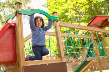Yakışıklı, hareketli küçük çocuk dışarıda oyun oynarken ve tırmanırken eğleniyor. Çocuklar okulda ya da anaokulunun renkli bahçesinde oynarlar. Çocuklar için sağlıklı yaz etkinliği.