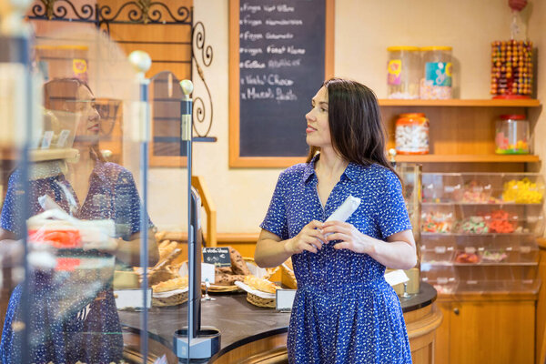Young pretty woman shopping in a bakery. A customer standing near a showcase with sweets in a store