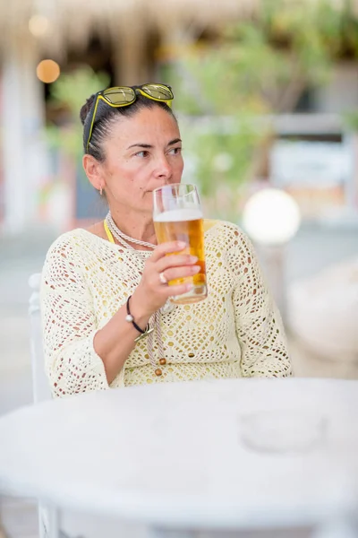 Portrait of beautiful young woman drinking beer at beach cafe and enjoying summer day