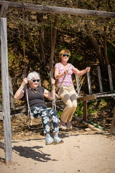 两个老年妇女高兴地挥动着秋千 还带着扇子 快乐退休的概念 — 图库照片