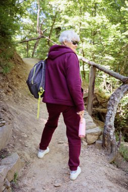 Orman yolunda yürüyüş yapan yaşlı bir kadın. Eğlence ve sağlıklı yaşam tarzı, ilham verici doğa. Fitness ve yürüyüş ve aktivite konsepti.