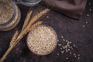 Kurutulmamış organik arpa gevreği, beyaz ahşap arka planda buğday kulakları olan bir kasede. Sağlıklı ve diyet gıda konsepti.