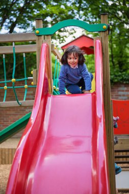 Yakışıklı, hareketli küçük çocuk dışarıda oyun oynarken ve kayarken eğleniyor. Çocuklar okulda ya da anaokulunun renkli bahçesinde oynarlar. Çocuklar için sağlıklı yaz etkinliği.
