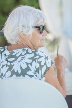Portrait of attractive senior woman sitting in a summer outdoor cafe and drinking coffee