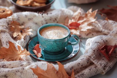 Sonbahar kompozisyonu beyaz örgü eşarp, mavi fincan kahve ve masada kuru sarı yapraklar. Sonbahar havası.
