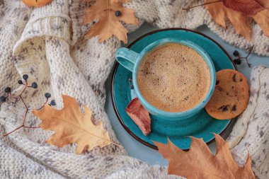 Sonbahar kompozisyonu beyaz örgü eşarp, mavi fincan kahve, kurabiye ve masada kuru sarı yapraklar. Sonbahar havası.