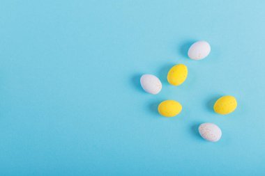 Minimalistic easter background of chocolate candy yellow and white eggs on a blue background