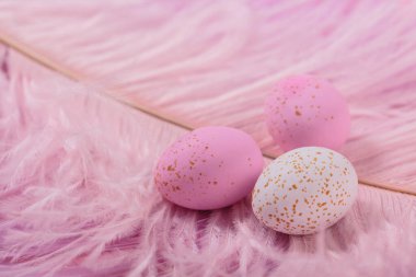 Easter candy chocolate eggs and almond sweets lying on pink feathers background. Happy Easter concept.