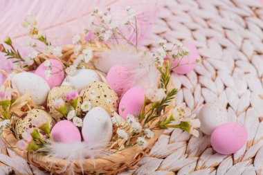 Easter candy chocolate eggs and almond sweets lying in a birds nest decorated with flowers and feathers on white background. Happy Easter concept.