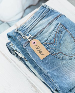 Bir yığın kot pantolon ve beyaz arka planda yazısız el işi kağıt etiket. İkinci el mağaza, bağış, satış, ikinci el.