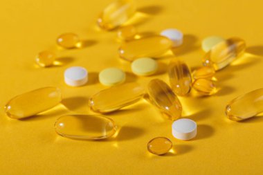 Diyet, beslenme, sağlıklı yeme konsepti. Türlü yağlar sarı softgel kapsülleri ve sarı arka planda gıda takviyesi hapları moda gölgeler ve yansımalarla dolu.