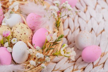Easter candy chocolate eggs and almond sweets lying in a birds nest decorated with flowers and feathers on white background. Happy Easter concept.