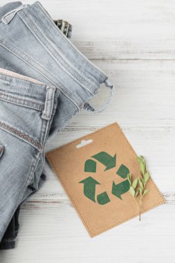 Mavi kot pantolon ve geri dönüşüm sembollü kağıt kartla sürdürülebilir bir hayat. İkinci el kıyafet fikri. Dairesel moda, bağış, yardım konsepti. Üst görünüm