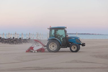 Evening empty beach. Tractor smoothes the sand on public beach by the sea