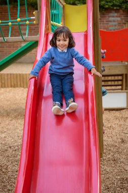 Yakışıklı, hareketli küçük çocuk dışarıda oyun oynarken ve kayarken eğleniyor. Çocuklar okulda ya da anaokulunun renkli bahçesinde oynarlar. Çocuklar için sağlıklı yaz etkinliği.