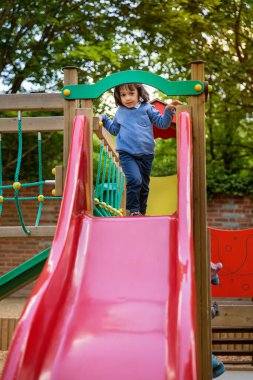 Yakışıklı, hareketli küçük çocuk dışarıda oyun oynarken ve kayarken eğleniyor. Çocuklar okulda ya da anaokulunun renkli bahçesinde oynarlar. Çocuklar için sağlıklı yaz etkinliği.