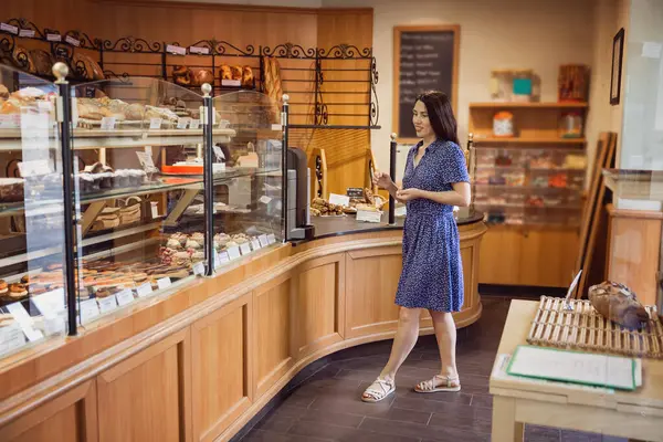 Stock image Young pretty woman shopping in a bakery. A customer standing near a showcase with sweets in a store