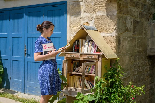 Woman takes the free books on the street. Pretty girl choosing a book to borrow in street library. Sidewalk Library box for public in Residential Neighborhood