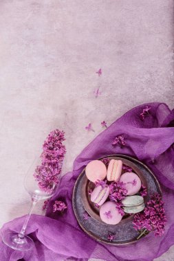 Tatlı pastel Fransız badem kurabiyeleri ve açık gri arka planda leylak çiçekleri. Pastane ve pastane için güzel bir kompozisyon. Kopyalama alanı olan üst görünüm