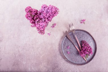 Açık gri arka planda eflatun çiçekli ve mor kumaşlı güzel bir masa. Restoranda romantik akşam yemeği için tatil süsü. Metin için kopyalama alanı olan üst görünüm