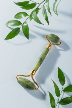 Masaj silindiri, açık mavi arka planda yeşil yapraklı ve yeşil taştan iki kafası olan yüz için. Güzellik yüz masajı terapisi, SPA kişisel bakım konsepti.