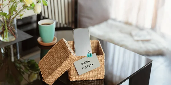 Smartphone is in separate wicker box with inscription digital detox on table. Refuse using digital gadgets at home in favor of live communication with your family