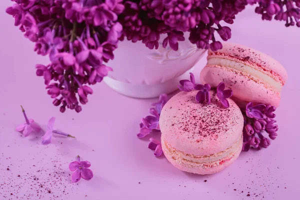 パステルカラーの甘いフランスのマカロンをピンクの背景にライラックの花で閉じます ベーカリーやペストリーショップのための美しい組成 — ストック写真