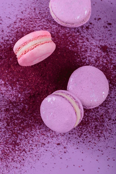 stock image Pastel colored sweet french macaroons and splash of dry blueberry powder on purple background. Beautiful composition for bakery and pastry shop, top view