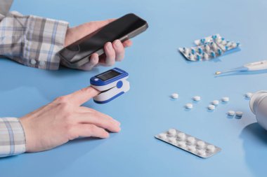 Dijital sağlık konsepti. Kadın, evdeki parmağında atım oksimetresinden gelen kan oksijeni seviyesini test ediyor ve akıllı telefondan sonuç çıkıyor.