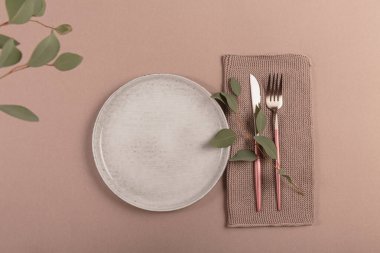 Kutlama masası. Gümüş modern çatal bıçak seti, okaliptüs dalı ve bej masa arka planındaki porselen plaka. Akdeniz düğünü ya da restoran menüsü konsepti. Düz yatış, üst görünüm