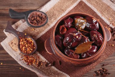 Bowl of pickled plums with spices on rustic wooden background. Clean eating, vegetarian food concept